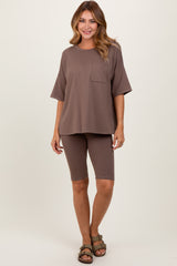 woman wearing a taupe oversized t-shirt with a pocket and matching bike shorts, standing against a neutral background
