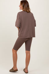woman wearing a brown oversized top and matching biker shorts, standing with her back to the camera