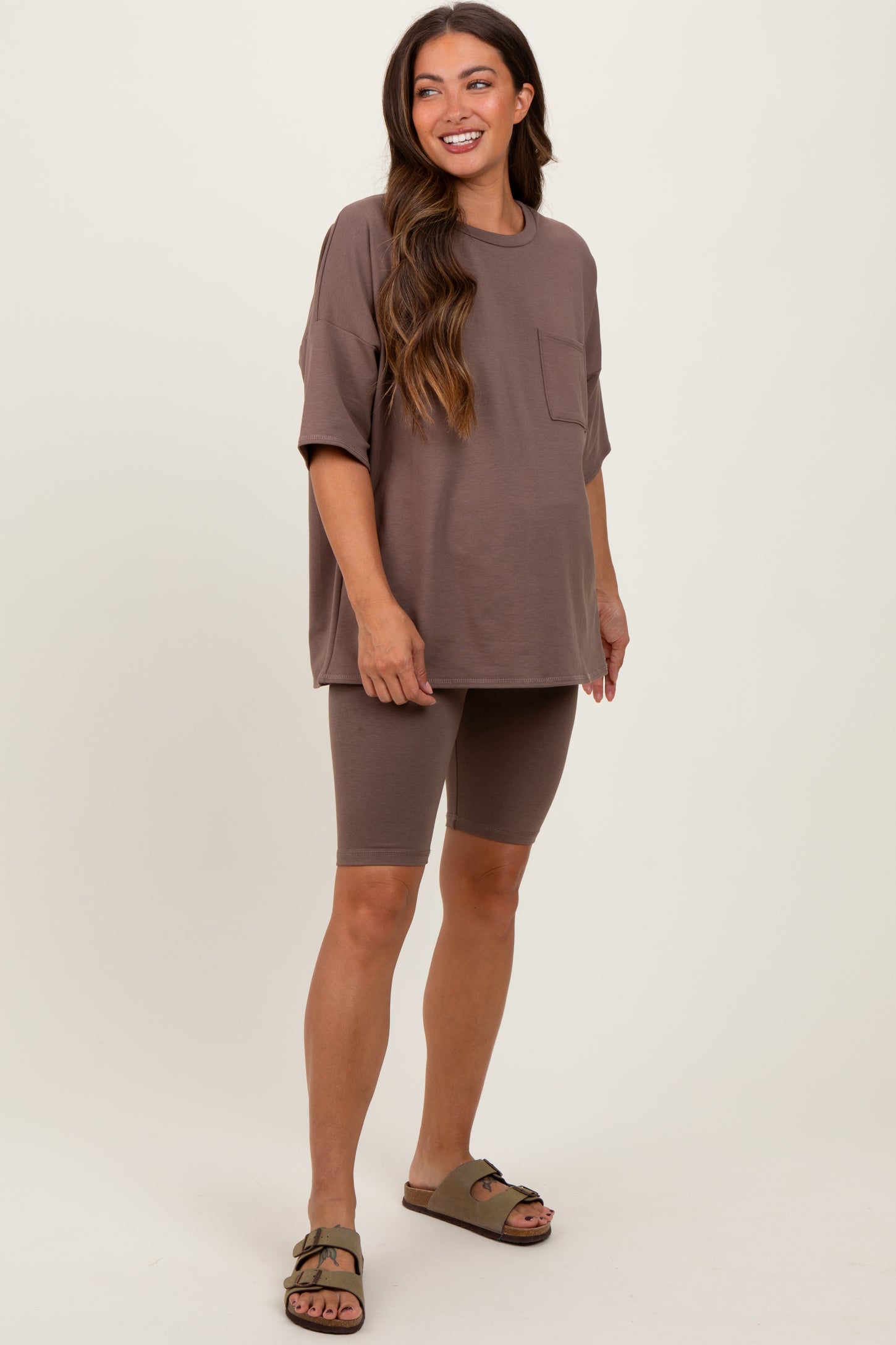 woman wearing a brown oversized maternity t-shirt and matching bike shorts, posing with one hand on her hip