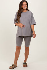 woman wearing a gray maternity oversized top with pocket and matching bike shorts, holding her baby bump