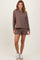 woman wearing a brown hooded sweatshirt with a front pocket and matching brown shorts, styled with white sneakers