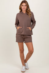 woman wearing a brown lightweight hoodie with pockets and matching brown shorts, standing on a neutral background