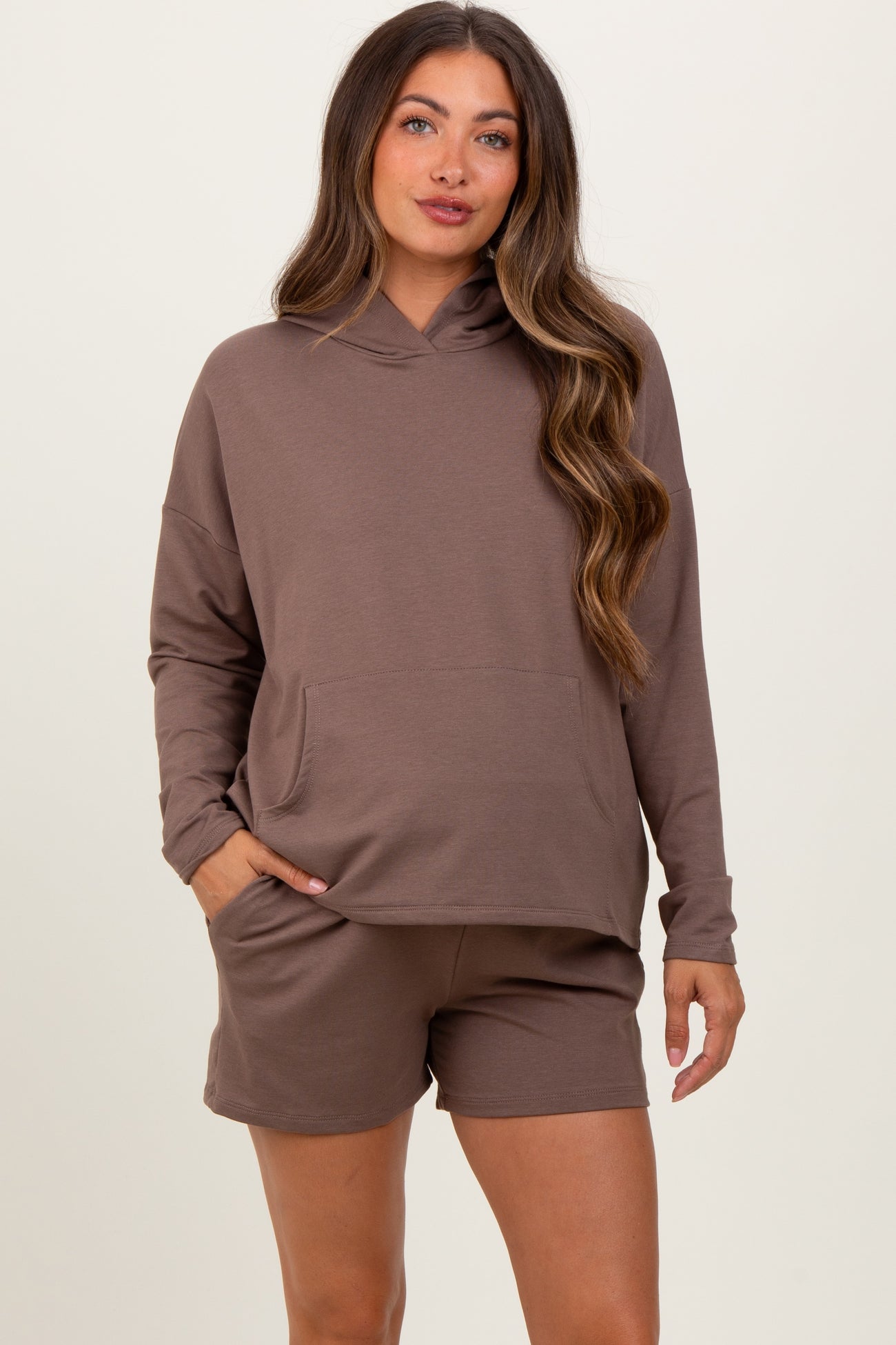 woman wearing a taupe maternity hoodie with a front pocket and matching shorts, showing her baby bump