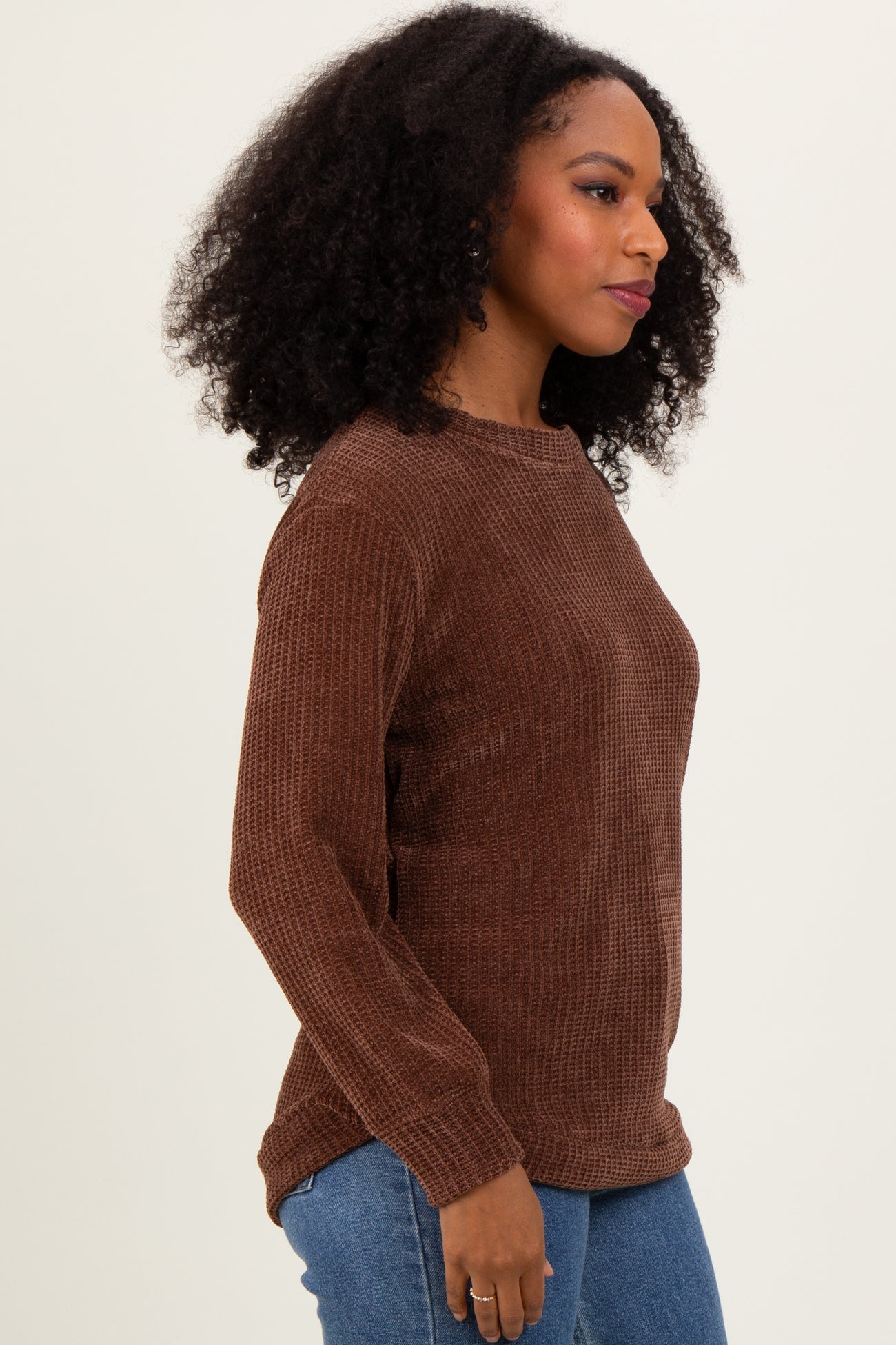 woman wearing a brown long sleeve textured top paired with blue jeans
