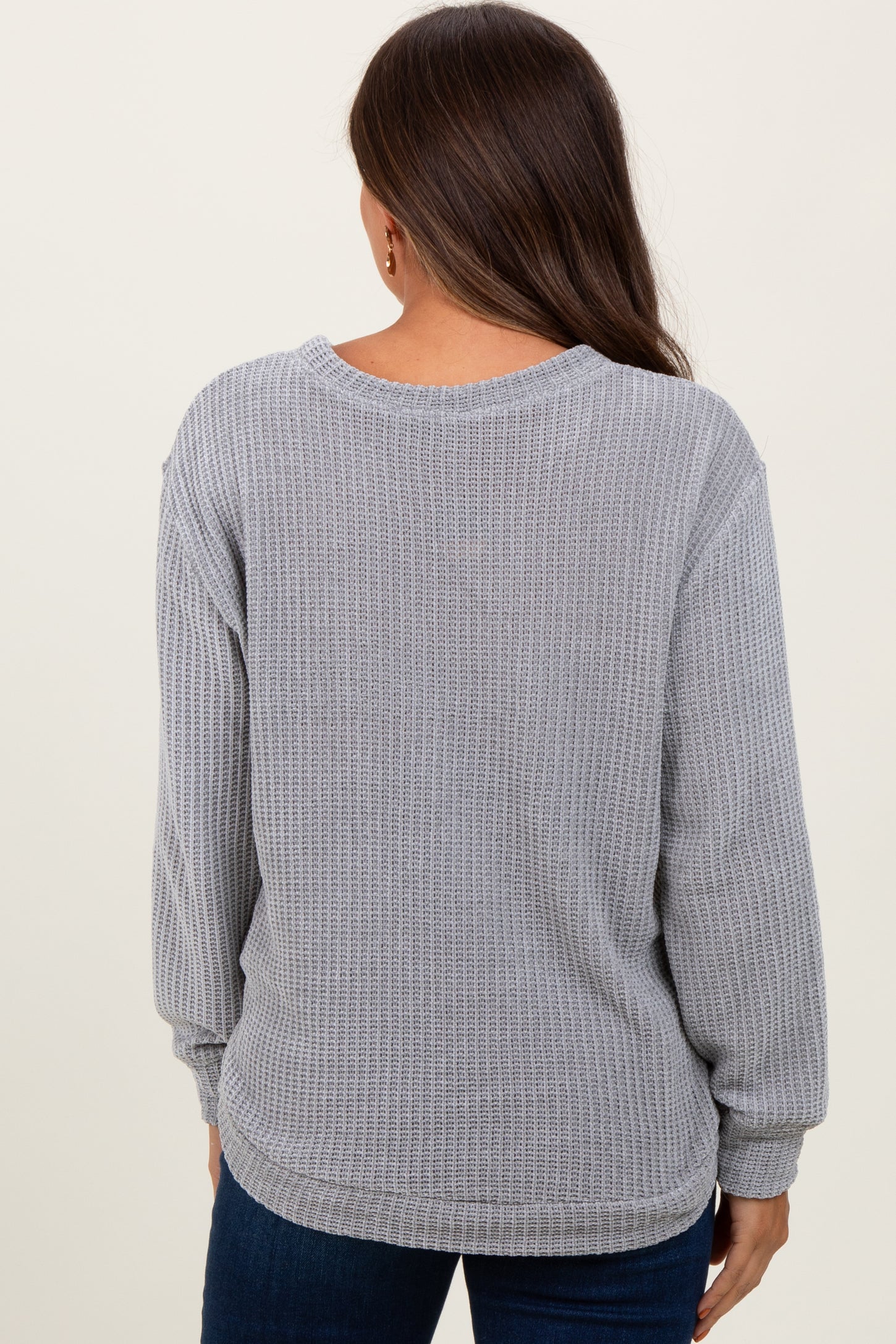 woman wearing a gray long sleeve maternity waffle knit top, showing the back view and styled with blue jeans