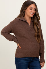 woman wearing a brown zip-up maternity sweater and showing her baby bump, styled with blue jeans