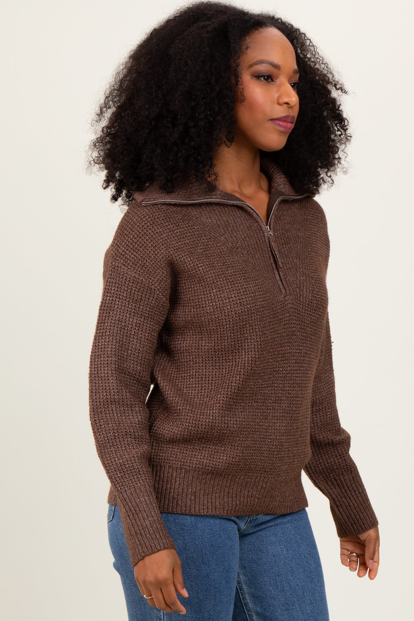 woman wearing a brown half-zip sweater with a textured design and ribbed hem, paired with blue jeans