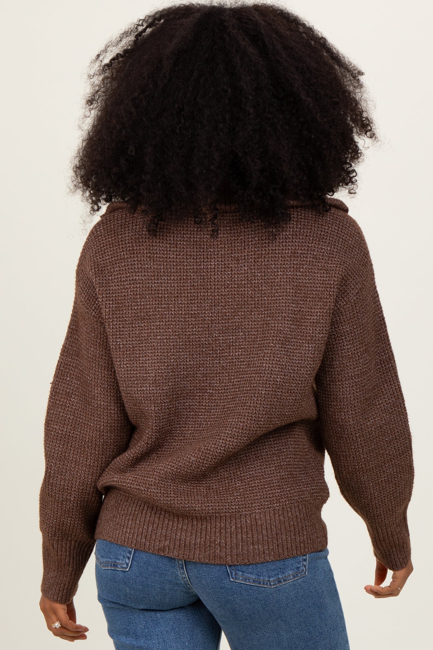 woman wearing a brown oversized knit sweater and blue jeans, seen from the back