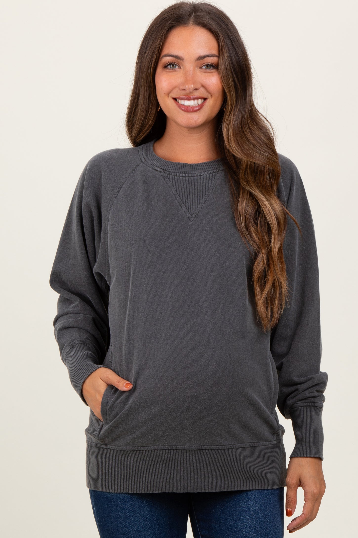 woman wearing a dark gray maternity sweatshirt with side pockets and raglan sleeves, showing a baby bump