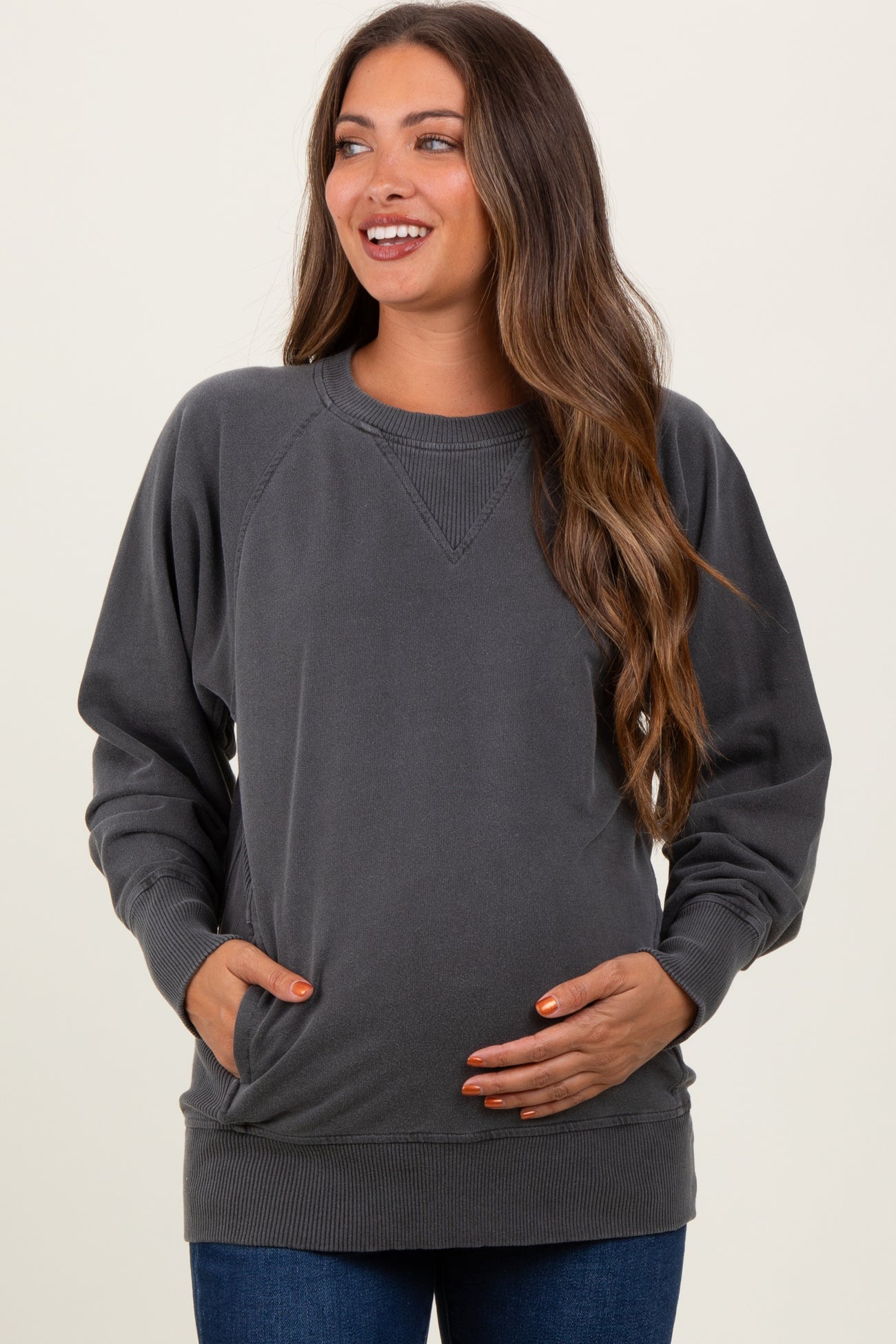 woman wearing a charcoal gray maternity sweatshirt with a relaxed fit and pockets, holding her baby bump