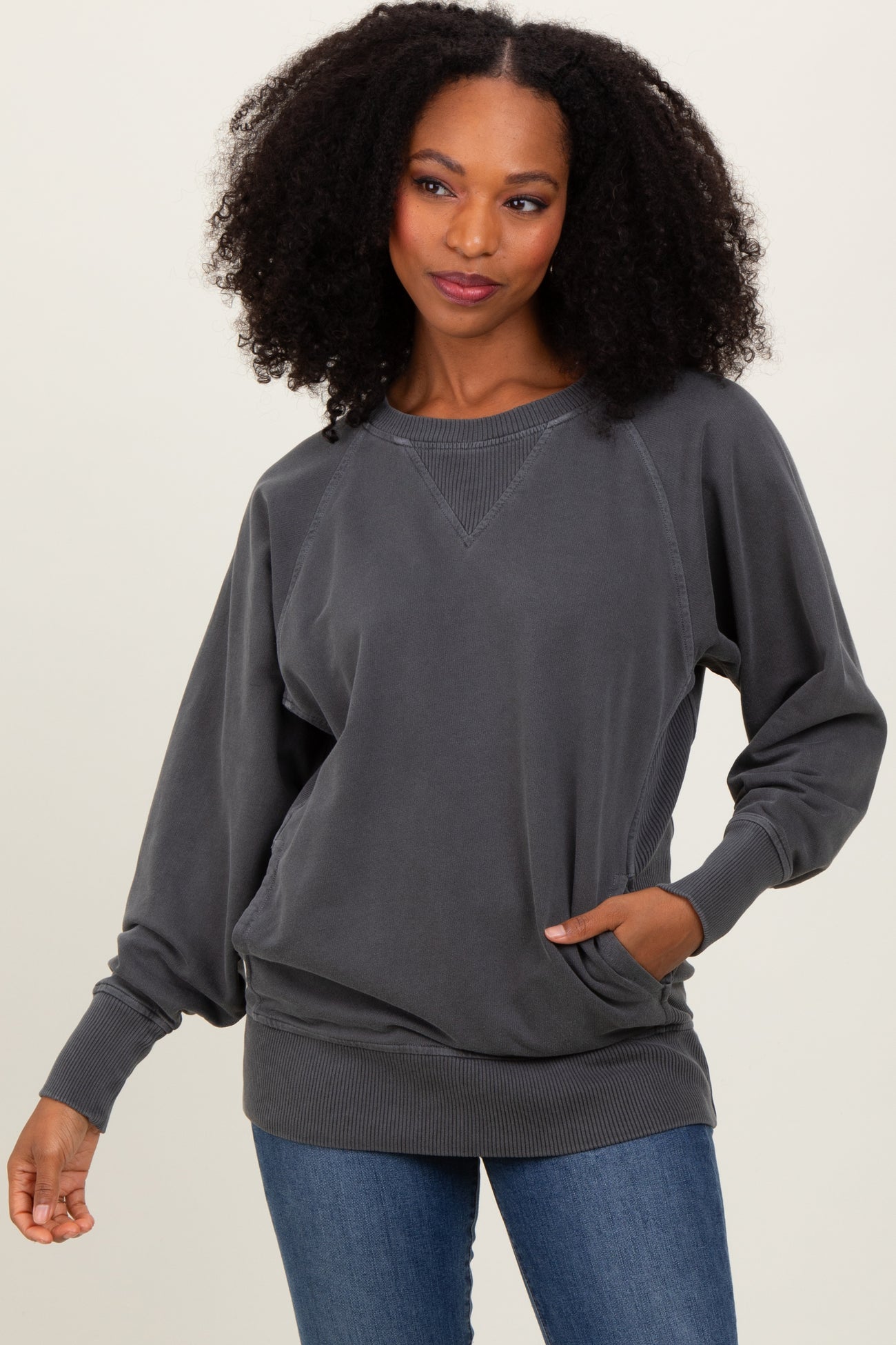 woman wearing a gray oversized sweatshirt with raglan sleeves and side pockets, styled with blue jeans