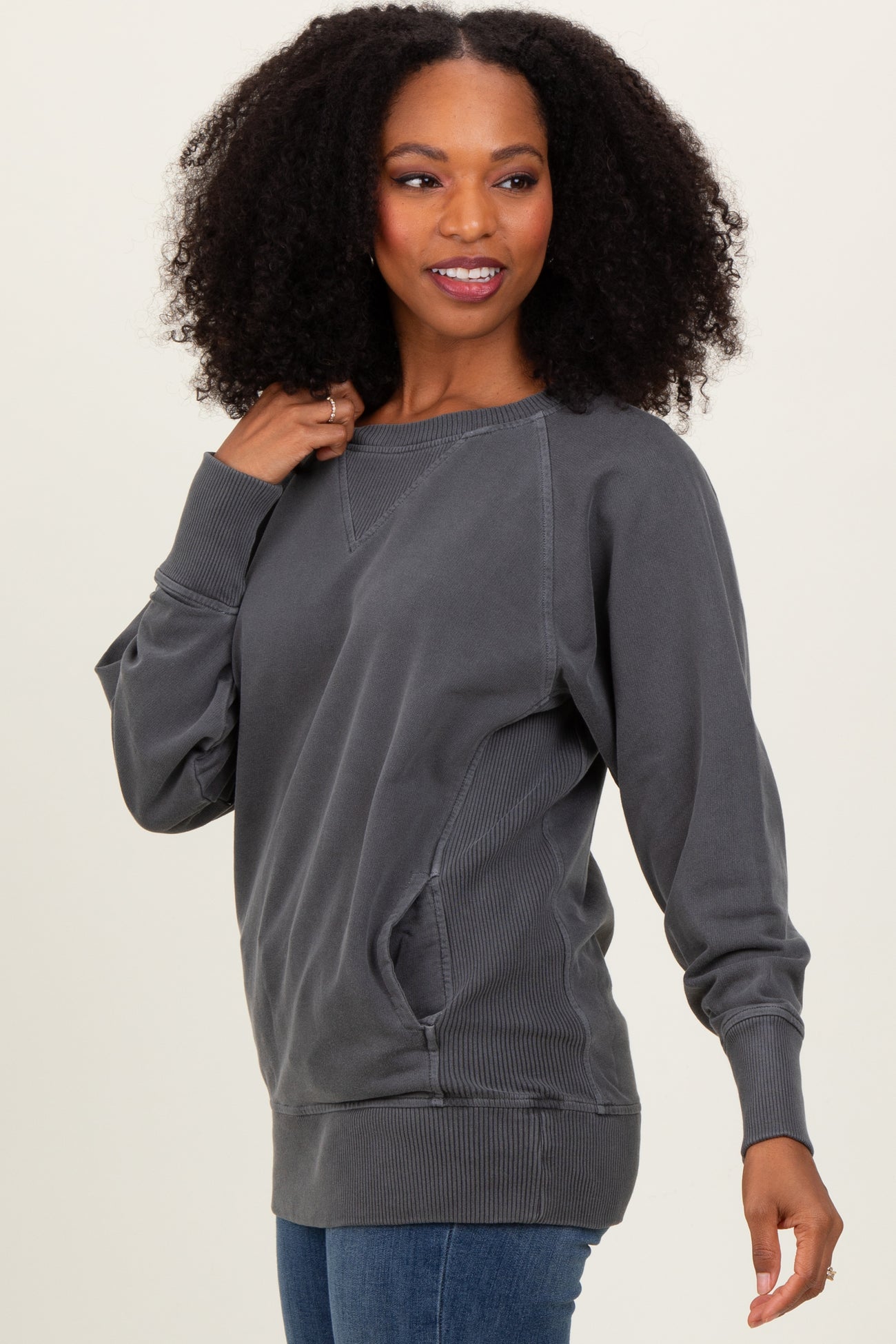 woman wearing a dark gray oversized sweatshirt with side pockets and ribbed hem, styled with blue jeans