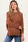 woman wearing a rust brown sweater with a relaxed fit and side slits, styled with blue jeans