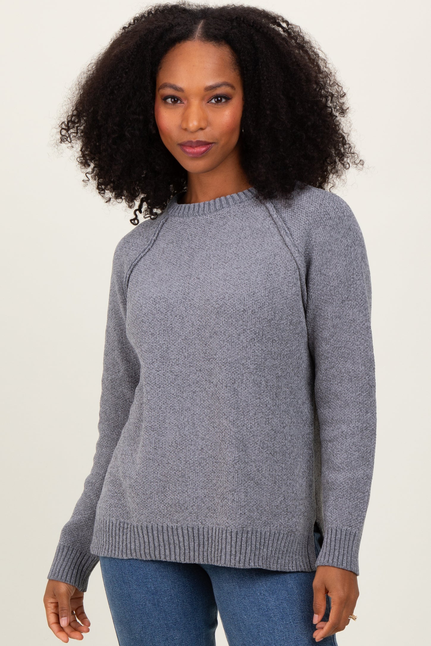woman wearing a grey knit sweater with a ribbed hem and side slits, paired with blue jeans