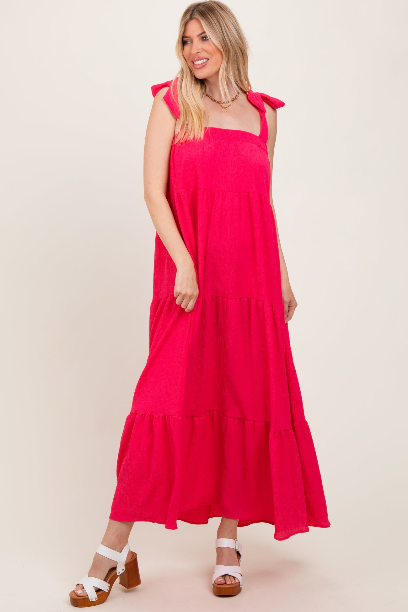 woman wearing a bright pink maxi dress with tie shoulder straps and a tiered design