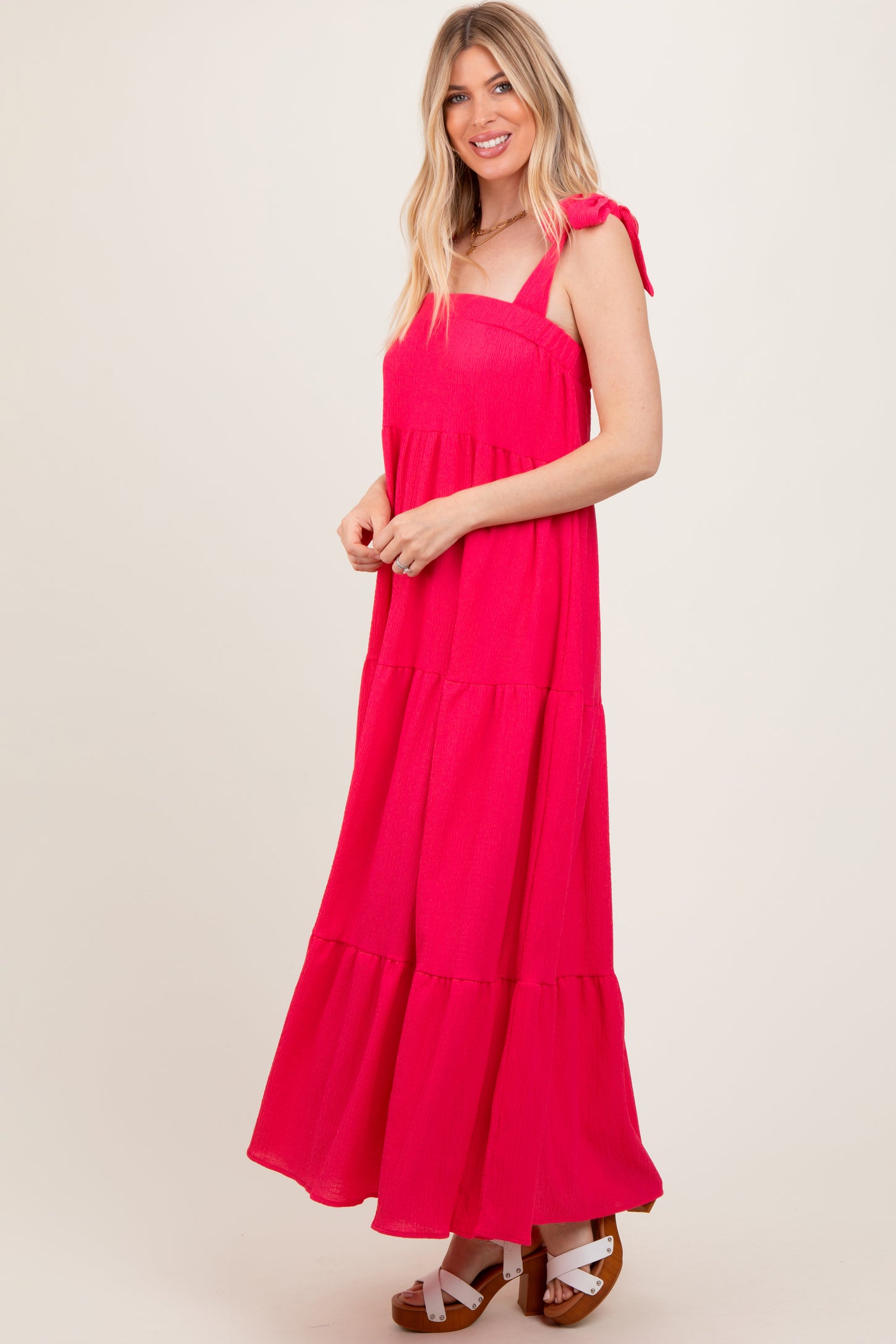 woman wearing a bright pink tiered maxi dress with tie straps and white platform sandals
