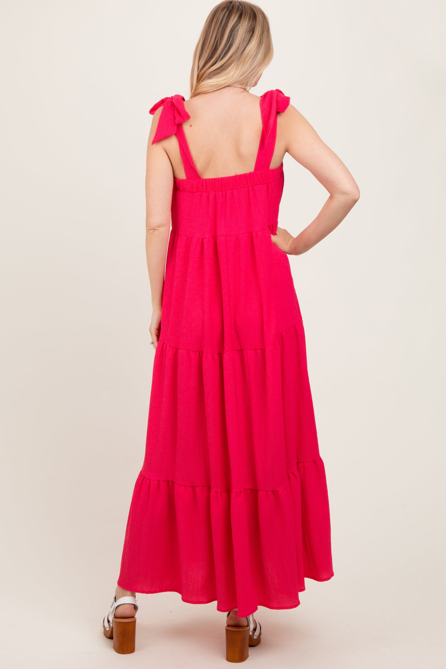 woman wearing a bright pink maxi dress with tie shoulder straps and tiered ruffle skirt, shown from the back