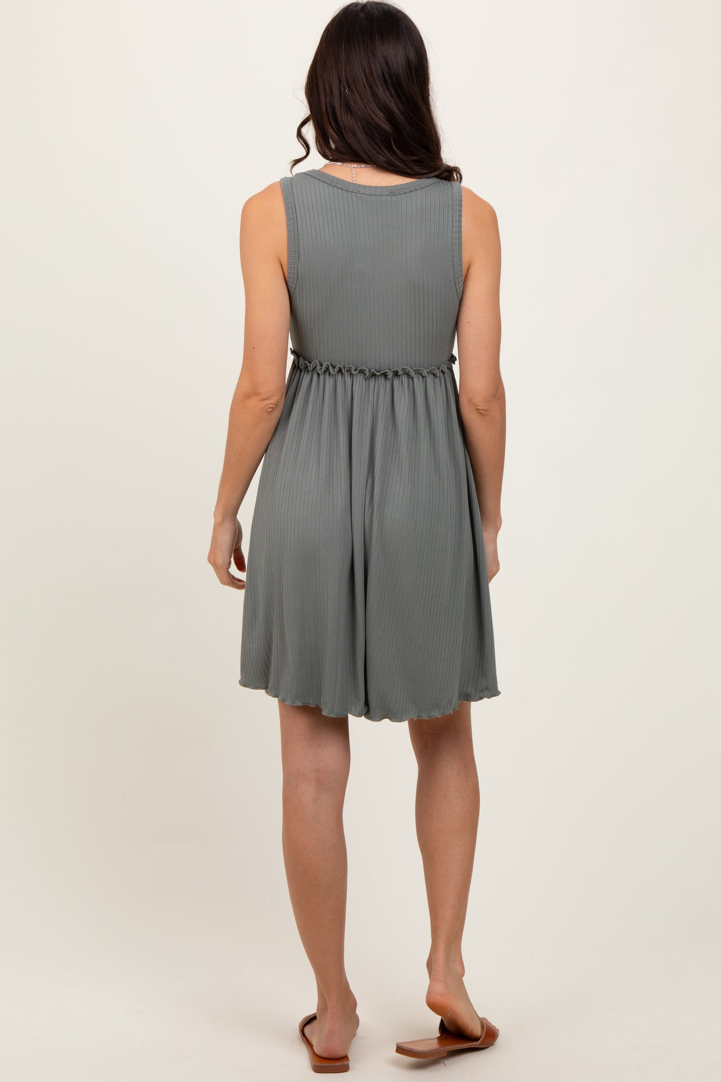 woman wearing a sleeveless light gray pleated dress with a cinched waist and flowing skirt, seen from the back