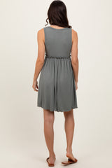 woman wearing a sleeveless light gray pleated dress with a cinched waist and flowing skirt, seen from the back