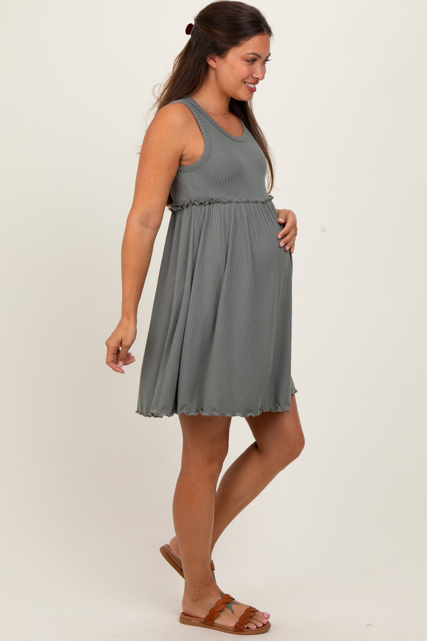 woman wearing a light gray maternity dress with a ribbed texture and ruffled hem, holding her baby bump