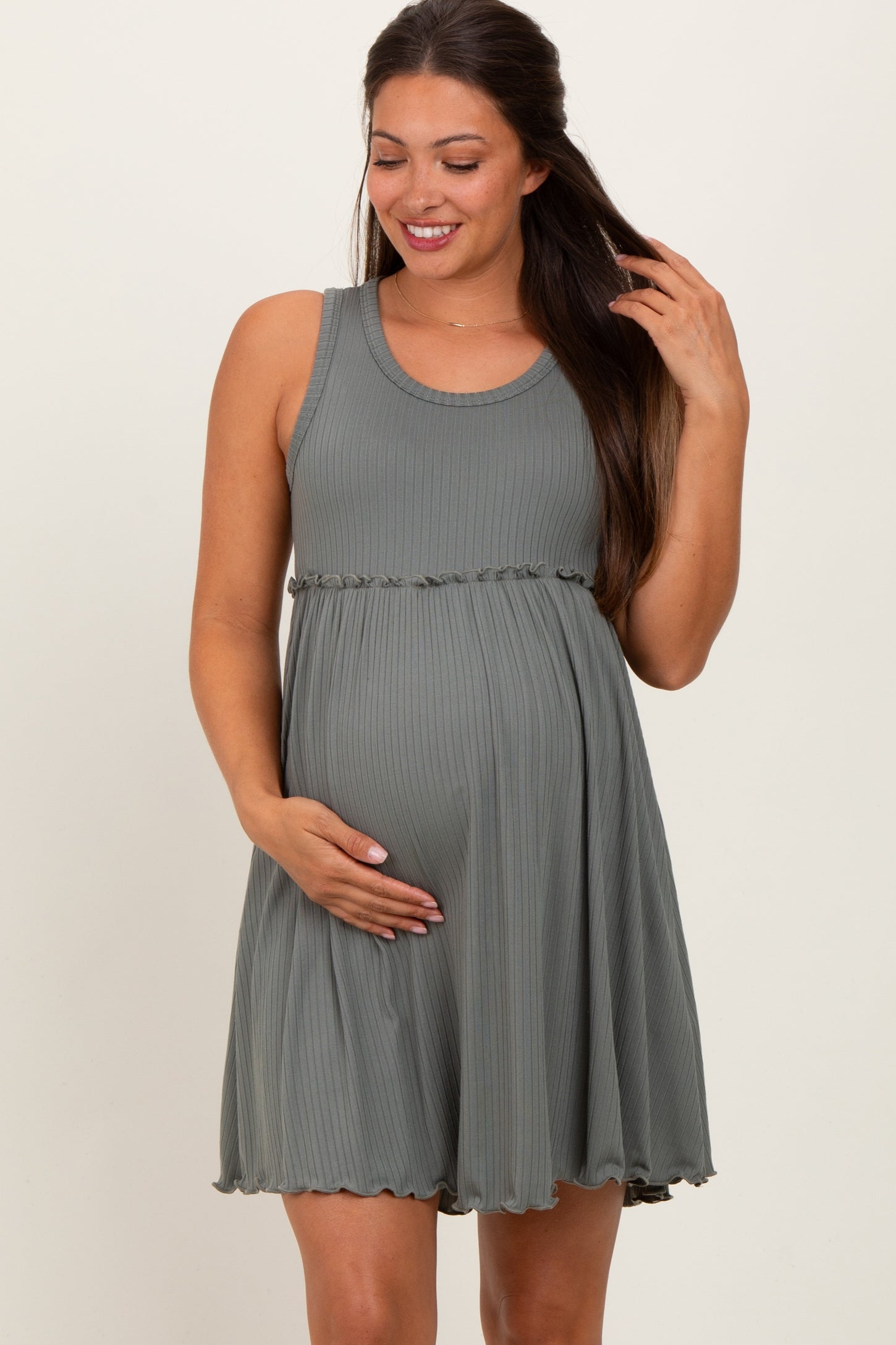 woman wearing a green ribbed maternity dress with a ruffled hemline and holding her baby bump