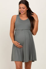 woman wearing a green ribbed maternity dress with a ruffled hemline and holding her baby bump