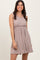 woman wearing a taupe sleeveless pleated dress with a fitted bodice and flared skirt
