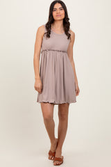 woman wearing a taupe sleeveless dress with a ruched waistline and a flowy skirt, standing and smiling