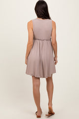 woman wearing a taupe sleeveless pleated dress with a gathered waist, shown from the back