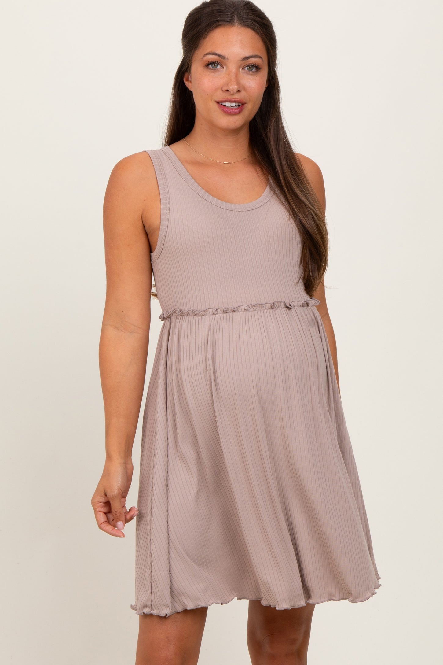woman wearing a taupe maternity dress with a scoop neckline and ruffle hem, highlighting her baby bump