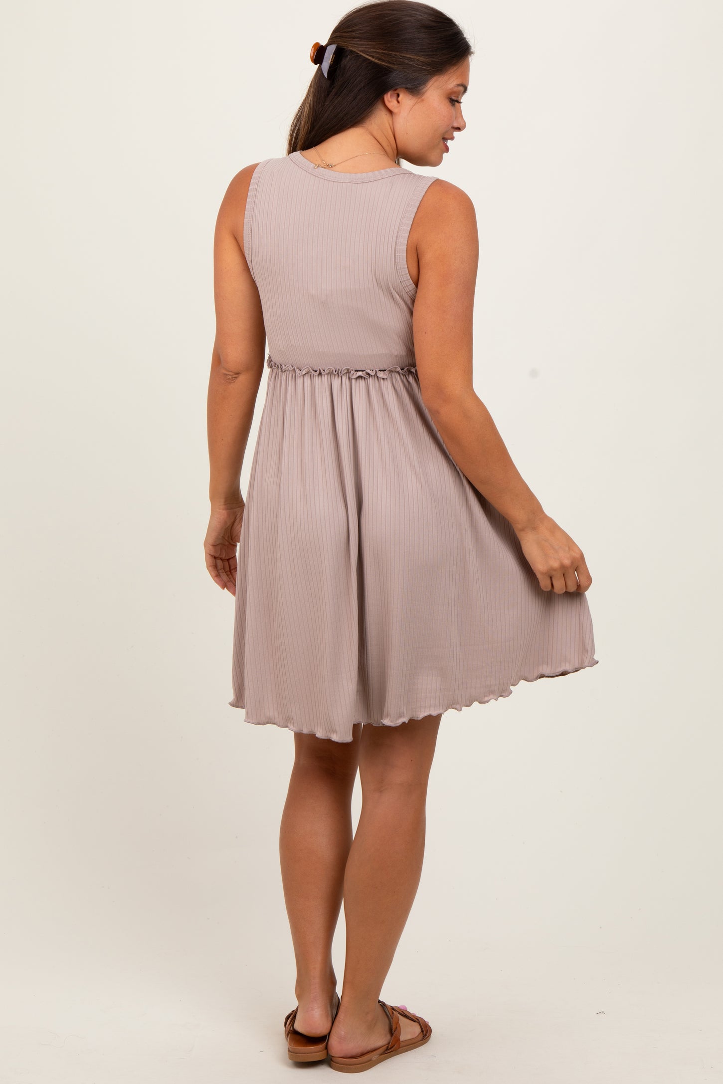 woman wearing a taupe sleeveless maternity dress with a fitted waist and flared skirt, showing a baby bump
