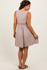 woman wearing a taupe sleeveless maternity dress with a fitted waist and flared skirt, showing a baby bump