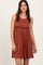 woman wearing a rust-colored pleated sundress with a fitted waist and flared skirt