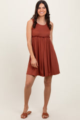 woman wearing a rust sleeveless pleated dress with a fitted bodice and flared skirt, standing and smiling