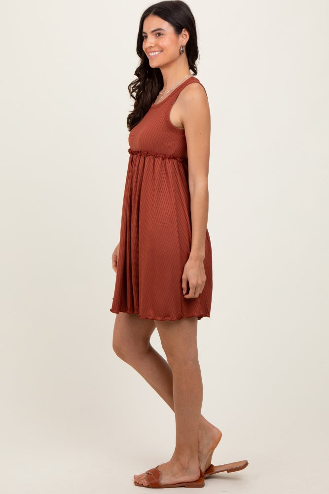 woman wearing a rust-colored sleeveless pleated swing dress with a waistline detail, standing with a relaxed pose