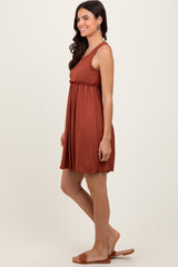 woman wearing a rust-colored sleeveless pleated swing dress with a waistline detail, standing with a relaxed pose