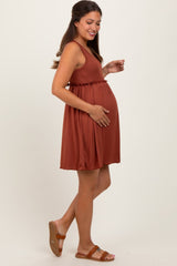 woman wearing a rust-colored maternity dress with a fitted bodice and flared skirt, holding her baby bump