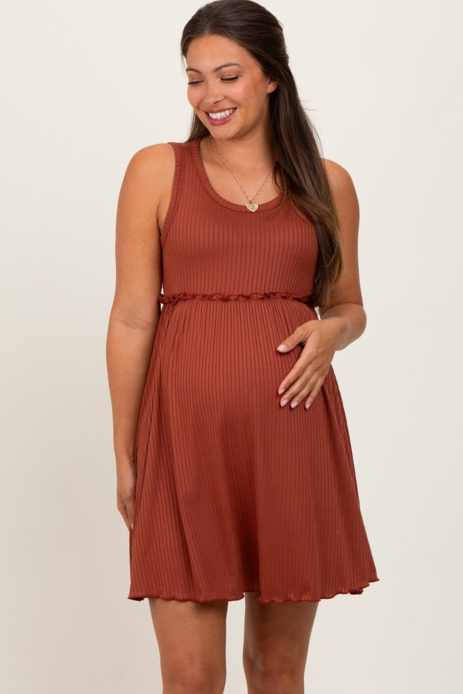 woman wearing a rust ribbed maternity dress with a ruffled waist and holding her baby bump