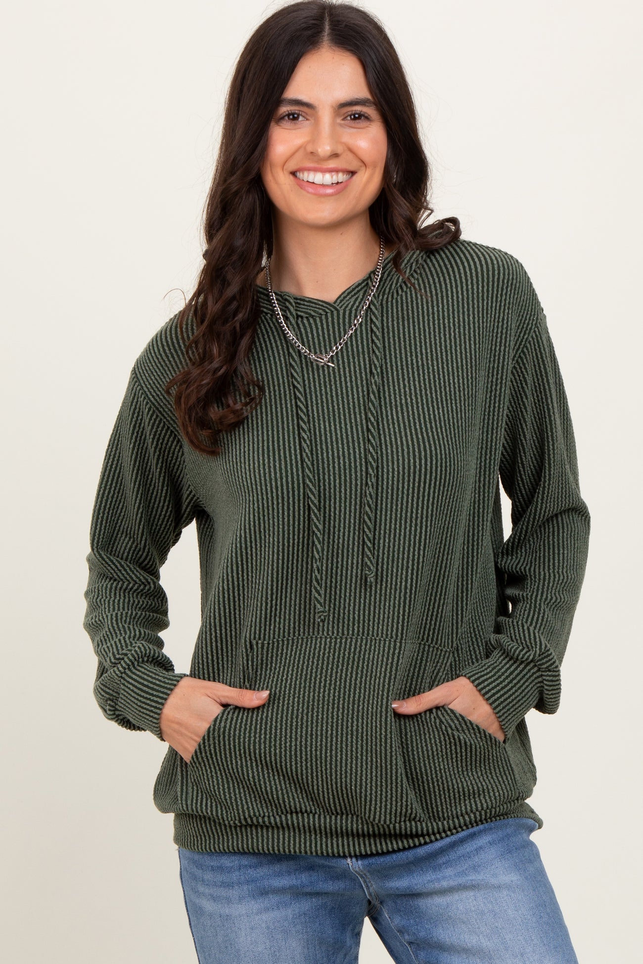 woman wearing a green striped hoodie with a front pocket and drawstring detail, smiling at the camera