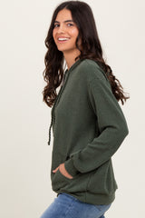 woman wearing a dark green textured hoodie with a front pocket and drawstring details