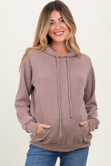 woman wearing a beige ribbed maternity hoodie with a front pocket and visibly holding her baby bump