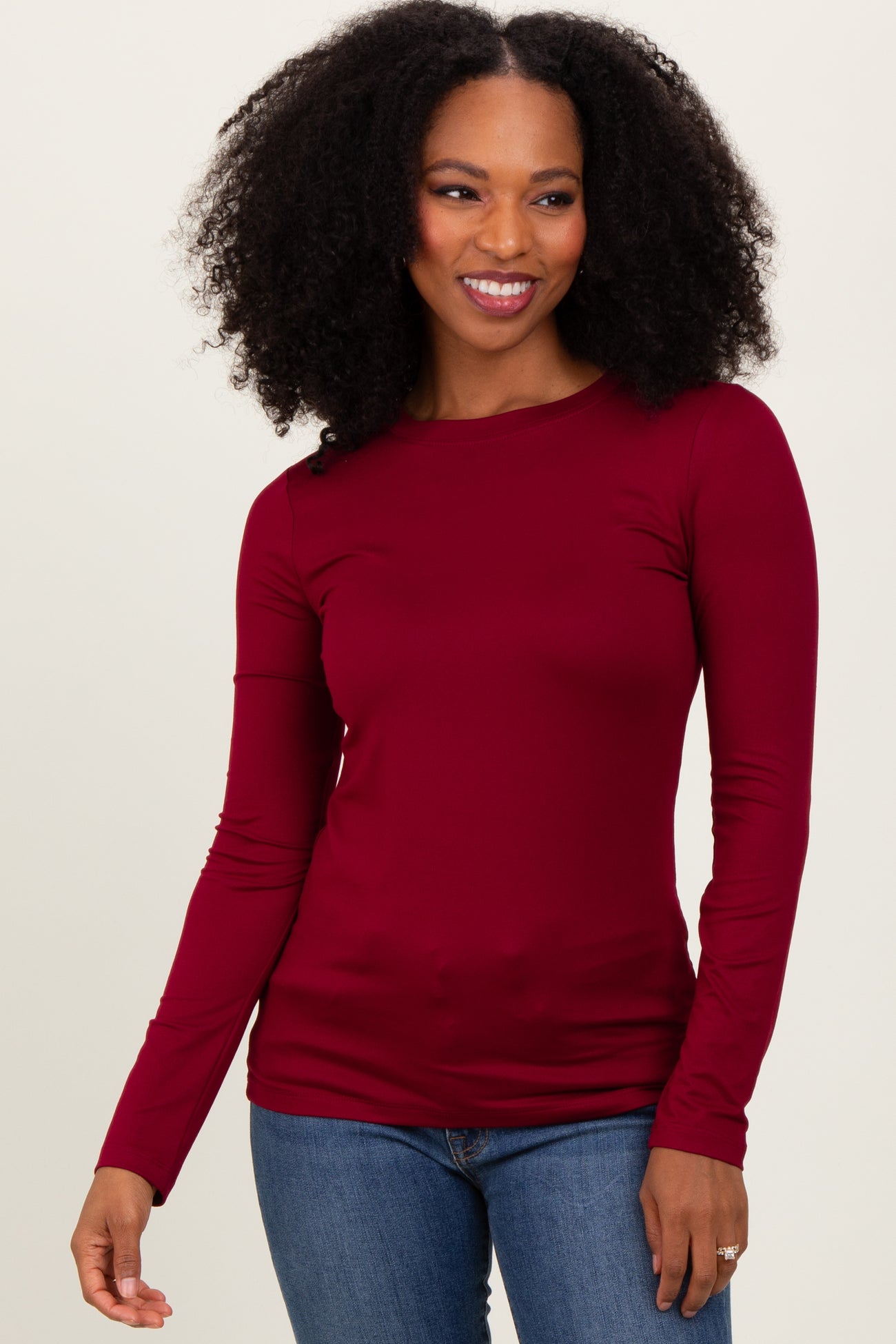 woman wearing a burgundy long sleeve top paired with blue jeans, smiling at the camera