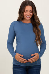 woman wearing a blue long sleeve maternity top and gently holding her baby bump