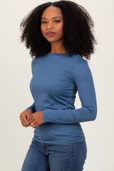 woman wearing a long sleeve blue top paired with denim jeans, standing confidently with her hands at her sides
