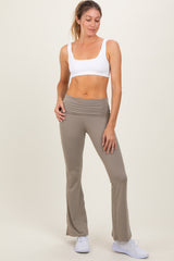 woman wearing a white sports bra and taupe flared leggings, posed confidently with one hand on her hip