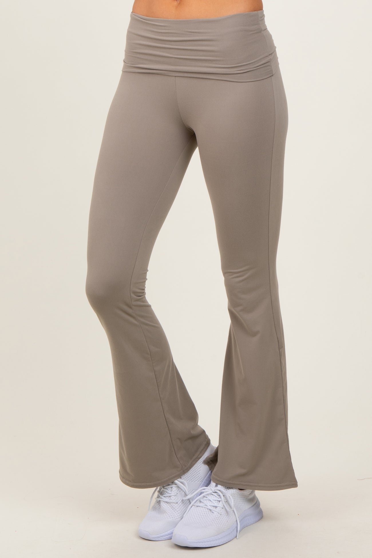 woman wearing light brown flared yoga pants paired with white athletic shoes on a beige background