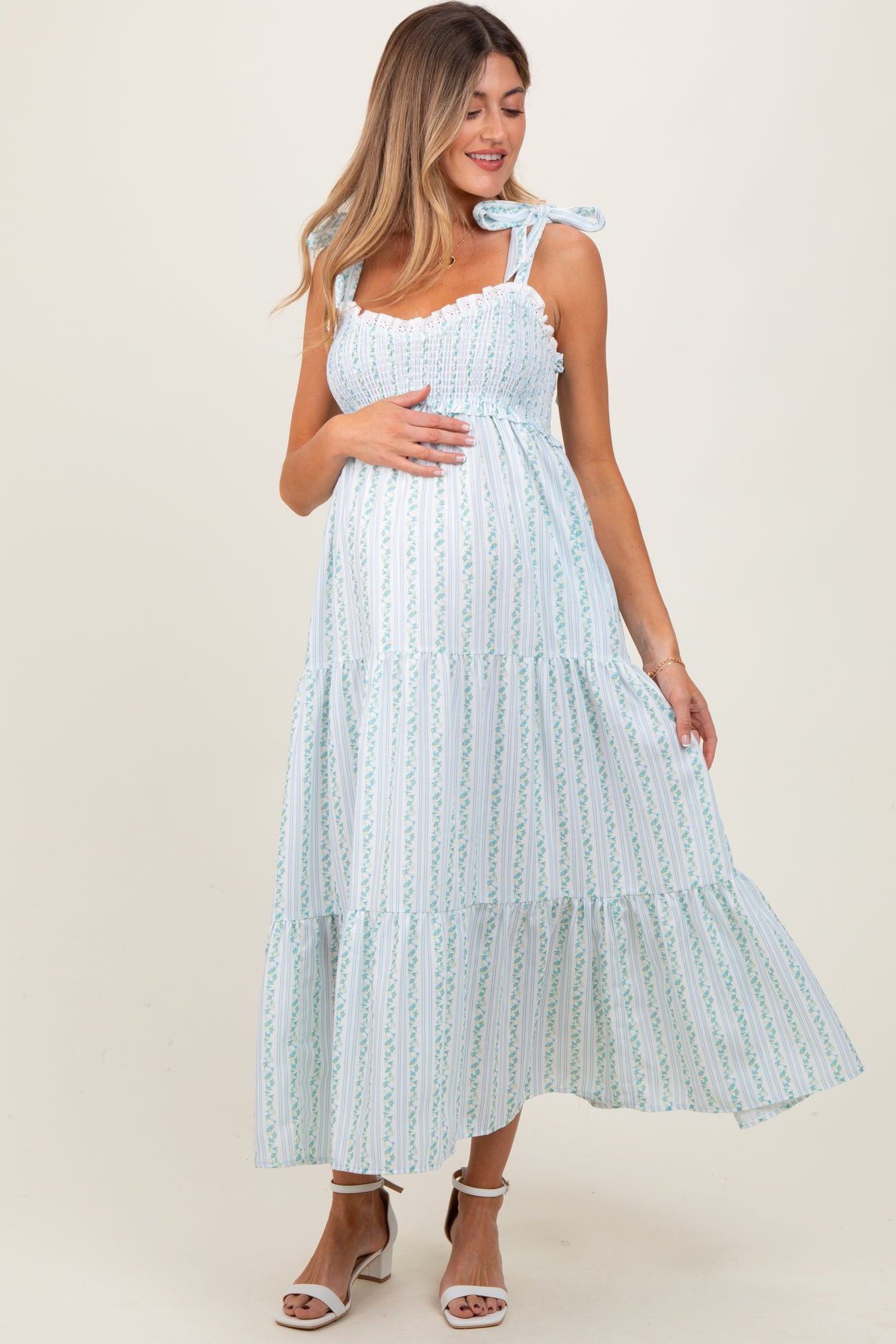 woman wearing a light blue and white striped maternity dress with ruffled tiers and bow straps, cradling her baby bump