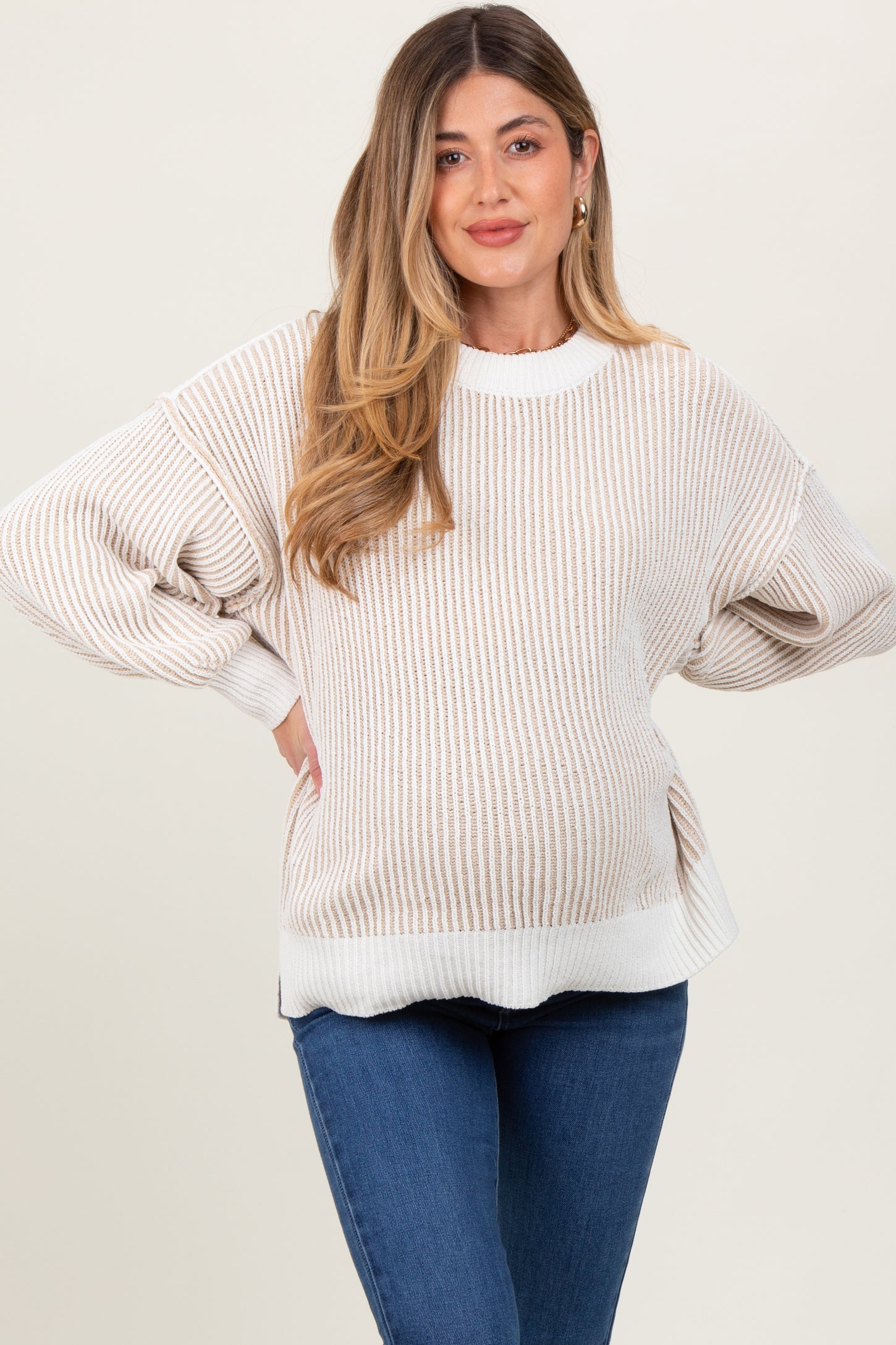 woman wearing a striped beige and white oversized maternity sweater with a visible baby bump and blue jeans