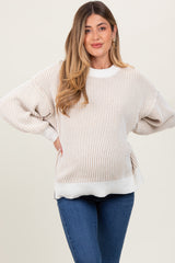 woman wearing a striped beige and white oversized maternity sweater with a visible baby bump and blue jeans