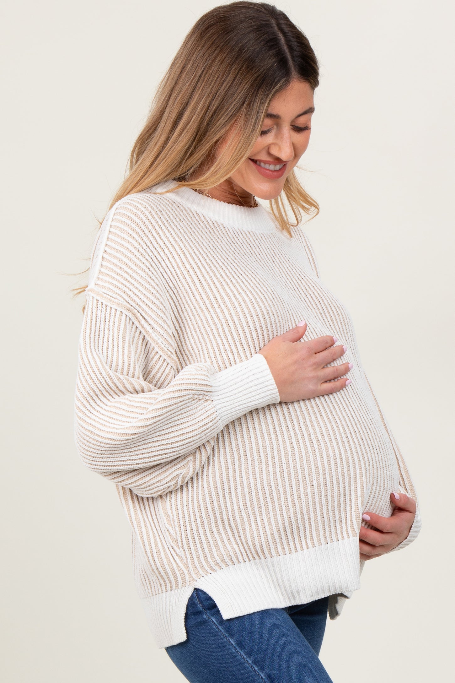 woman wearing a cream and beige striped maternity sweater and holding her baby bump